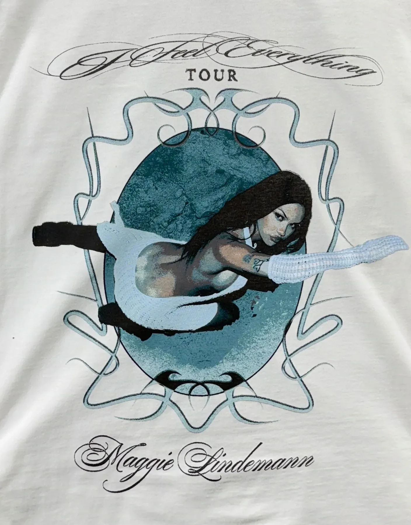 Front print: a teal oval held in chrome scrollwork, the tour lockup above it