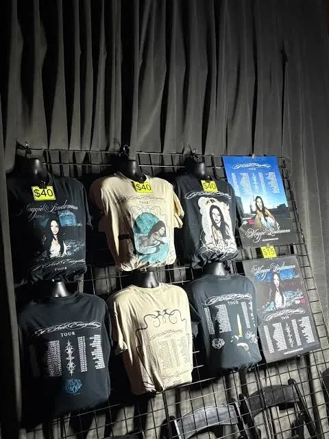 The merch wall at a Maggie Lindemann show: the three tour shirts hanging front and back, with price tags
