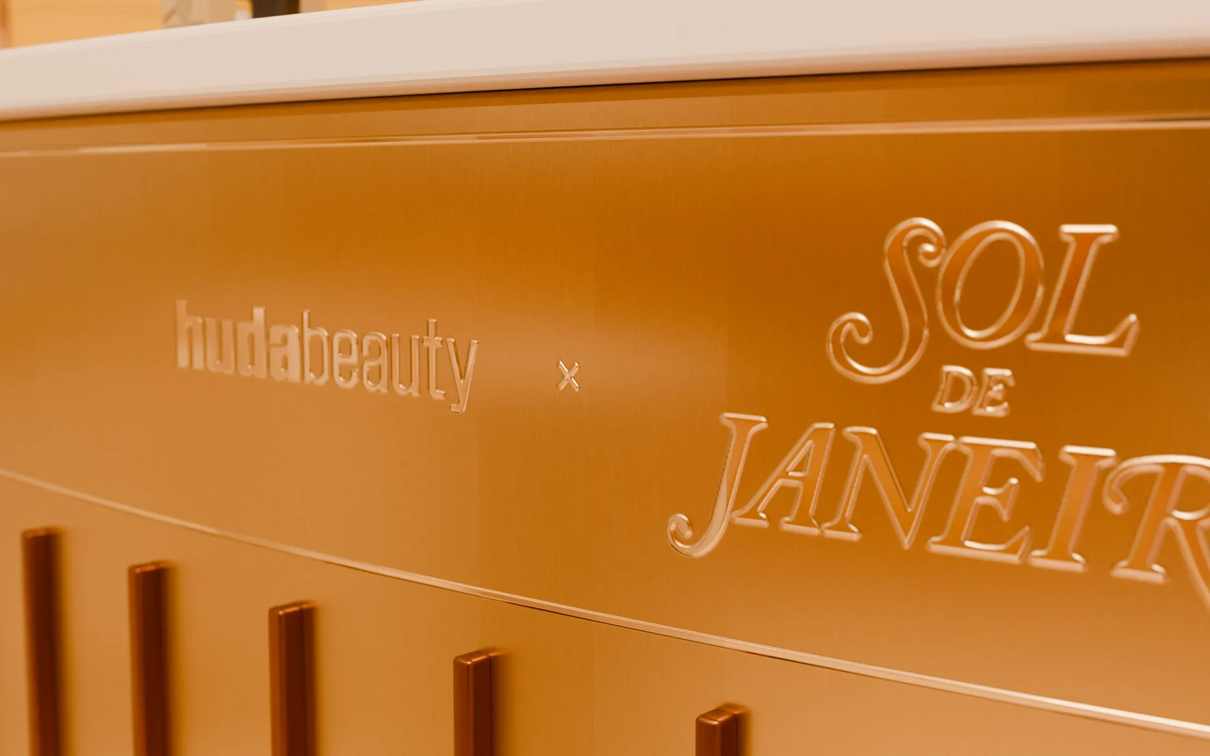 huda beauty × Sol de Janeiro engraved into the brushed brass of the testing counter