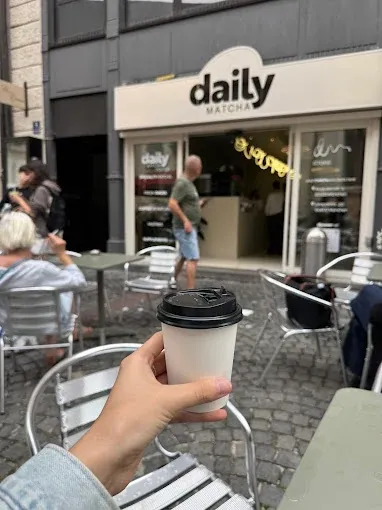 A Daily Matcha cup held in front of the shop